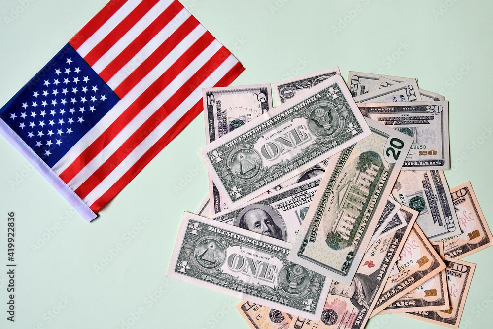 Pile of paper dollars and American flag. Banknotes of different denominations are scattered in random order. Top view. Close-up. Selective focus. Copy space. Pile of paper dollars and American flag. Banknotes of different denominations are scattered in random order. Top view. Close-up. Selective focus. Copy space.