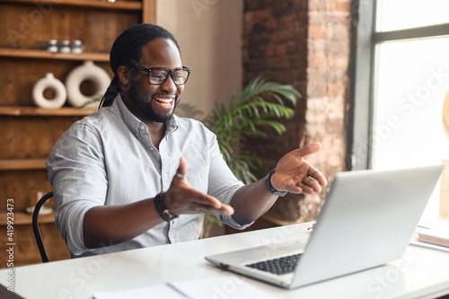 Foto Smiling African-American male office employee talking online, has video meeting,