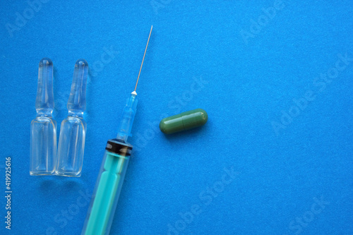 Syringe with needle, vials with medicine, tablets lie on blue background. Vaccination. Coronavirus. The concept of medicine and immunity. Vaccination against viral infections. Copy the space. Flatly.