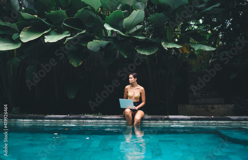 Fotografie, Obraz Female with laptop resting in pool in resort area
