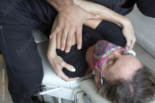 Woman with face mask lying on stretcher gets osteopath body adjustment. Anonymous physiotherapist pressing on female patient chest, physical theraphy treatment concept