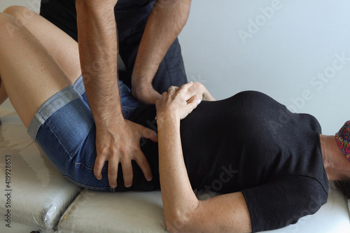 Anonymous osteopath working on hips of woman lying on stretcher. Doctor examination at office, health care concepts