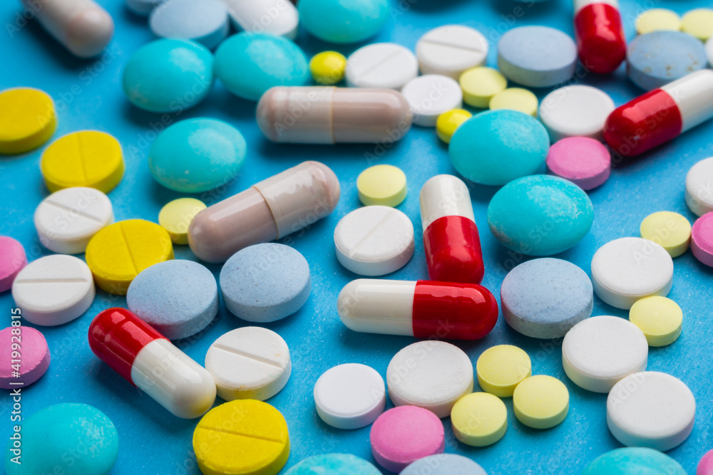 A lot of multicolored pills and capsules on a blue background as a concept of addiction from medicine. Vitamins to keep immunity on a high level. A lot of multicolored pills and capsules on a blue background as a concept of addiction from medicine. Vitamins to keep immunity on a high level.
