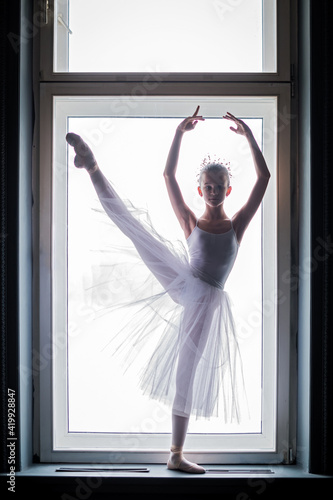 young slender ballerina in white tutu dances on pointe shoes in a spacious, bright room with large windows. photo