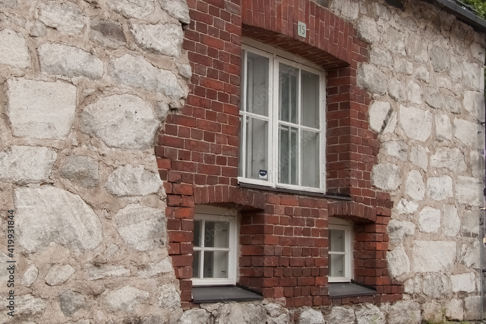 Одно большое и два маленьких окна в стене из красного кирпича и белого камня.