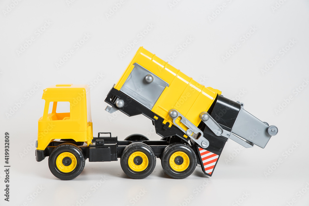 Plastic car. Toy model isolated on a white background. Yellow truck for the transport of garbage. Plastic car. Toy model isolated on a white background. Yellow truck for the transport of garbage.