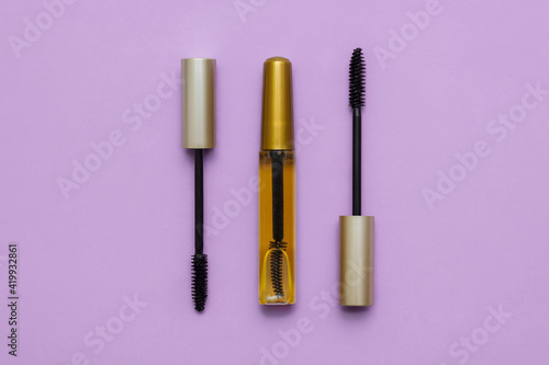 Two open black mascara and yellow oil for eyelashes and eyebrows with a brush on a pink background, flat lay, close-up, the concept of everyday makeup, care and treatment, women's cosmetic bag