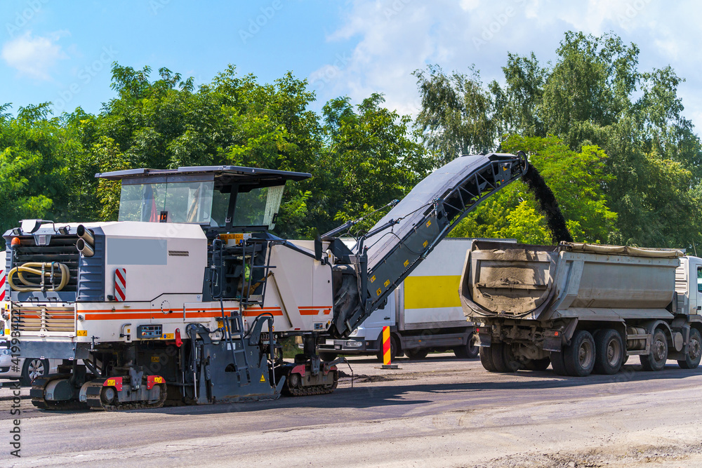 Big special machinery pours fresh asphalt out to smaller truck. New road construction. Selective focus.