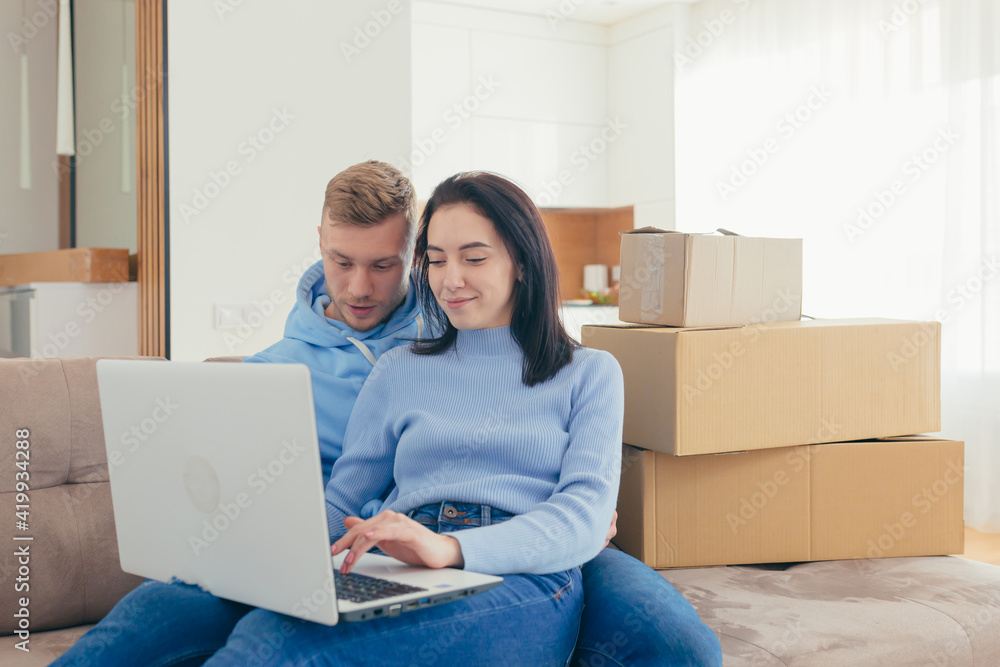 A couple in love with the newlyweds, moved to a new apartment, and use a laptop to choose new furniture for the apartment. make joint purchases online together