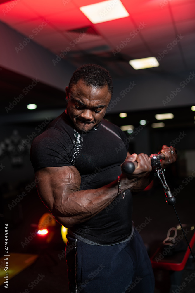 Sportsman in black sport clothes doing workout for hands and lifts weight on sport equipment. Muscular african american. Sportsman in black sport clothes doing workout for hands and lifts weight on sport equipment. Muscular african american.