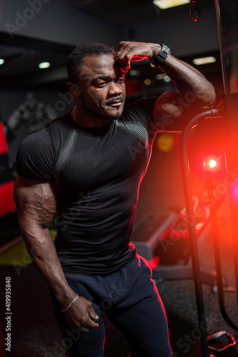 Concept photo of handsome african american athlete in black sport clothes near special equipment for training. Portrait of cute fitness trainer.