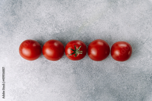 Line of red tomatoes on gray background