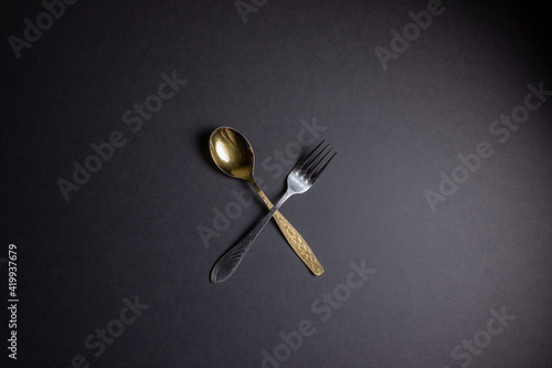 Gold spoon and silver fork on black background