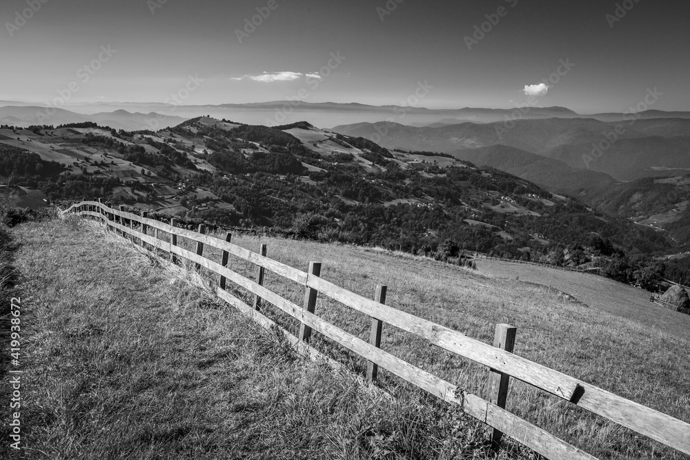 Long wooden fence along a mountain road protects the meadow. Black and white picture with a scenery hills landscape, Western Serbia