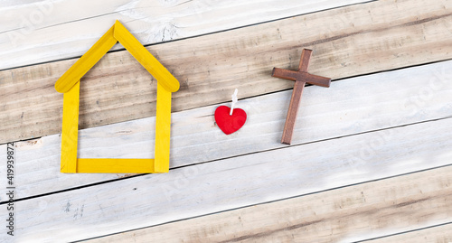 Heart and Wooden cross next to small yellow house wooden on white background. religion lifestyle concept.