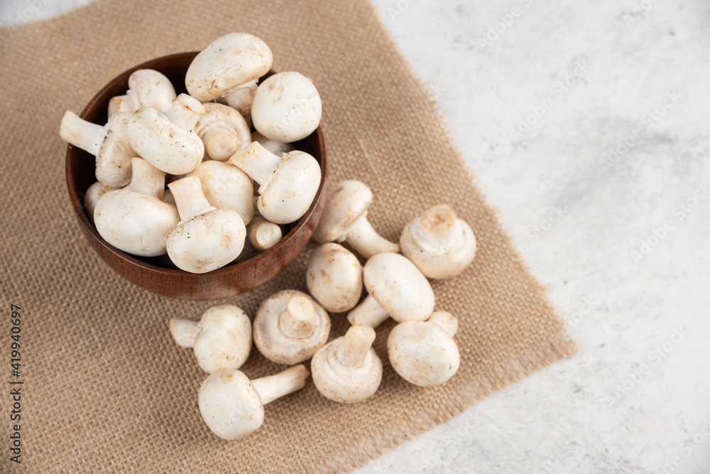 White mushrooms in a wooden cup on a piece of burlap