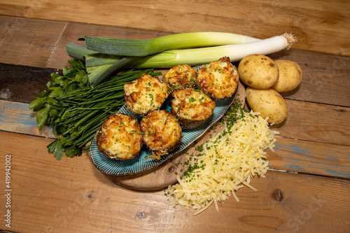 A selection of delicious Fish Pie Potato Skins topped with cheese and garnish on a wooden kitchen table background surrounded by the ingredients used to create the dish