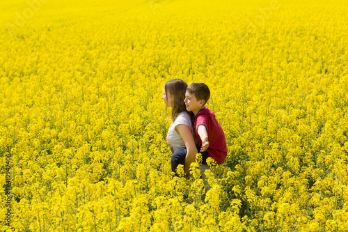 Pretty teenager girl with his little brother together enjoy the sunshine in the middle of a yellow flower field.