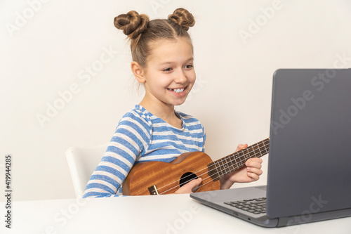 Girl sitting at home learns to play ukulele using online lessons