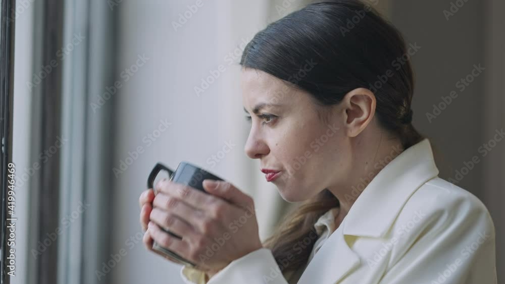 Side view face of relaxed young woman enjoying tea at lunch break looking out the window. Close-up portrait of happy smiling Caucasian businesswoman drinking hot drink and smiling. Slow motion. Side view face of relaxed young woman enjoying tea at lunch break looking out the window. Close-up portrait of happy smiling Caucasian businesswoman drinking hot drink and smiling. Slow motion.