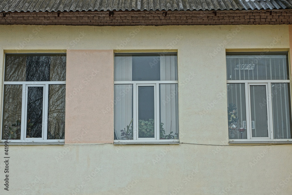 a row of three white windows on a brown concrete wall of a building on the street