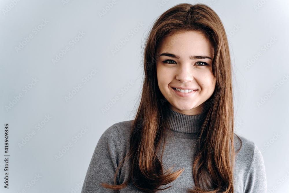 Close up view. Beautiful girl sincerely smiling on a gray background. Place for advertising, copy space.