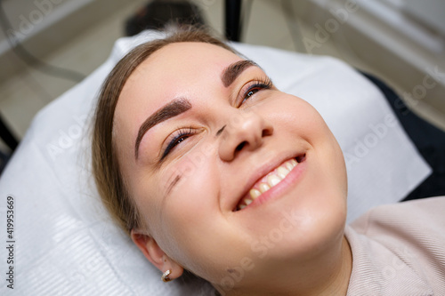 Woman with permanent makeup tattoo on her eyebrows. Close-up beautician makes makeup applies a foundation. Professional make-up and cosmetic skin care.