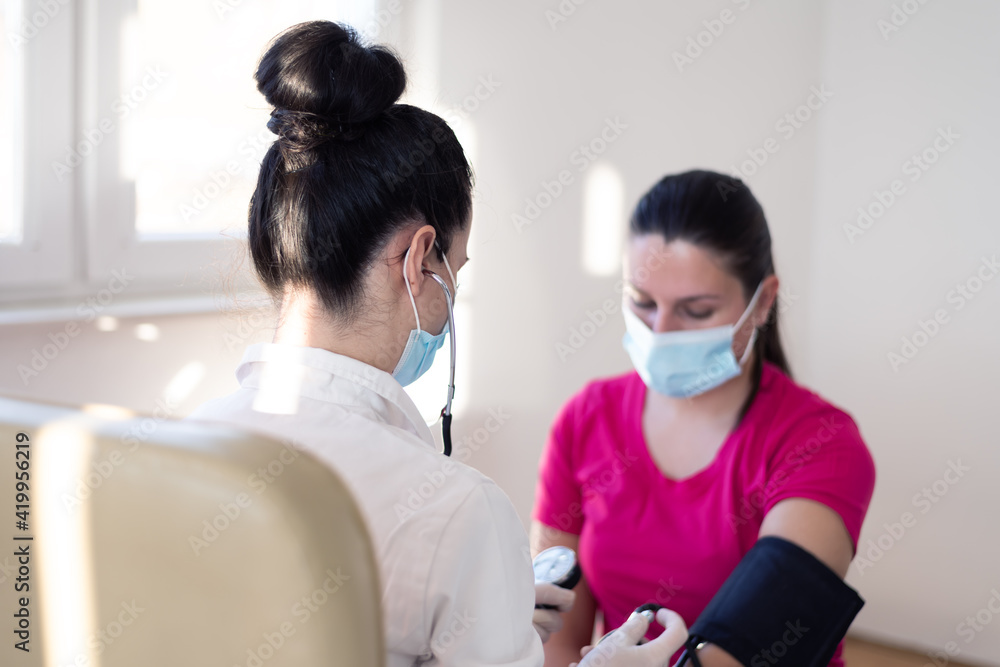 Female doctor using sphygmomanometer with stethoscope checking blood pressure to a patient in the hospital Female doctor using sphygmomanometer with stethoscope checking blood pressure to a patient in the hospital