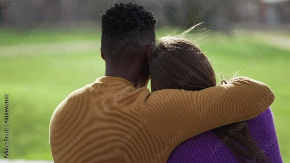 Back of interracial couple in embrace together at park bench Back of interracial couple in embrace together at park bench