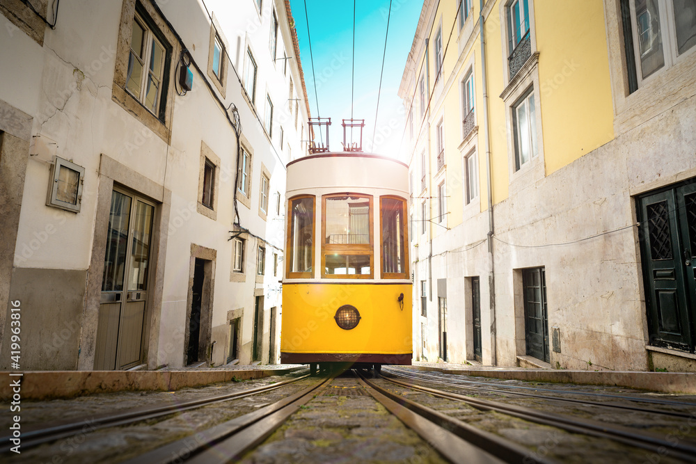 Trams in Lisbon city. Famous retro yellow funicular tram on narrow streets of Lisbon old town on a sunny summer day. Ascensor da Bica, Portugal
