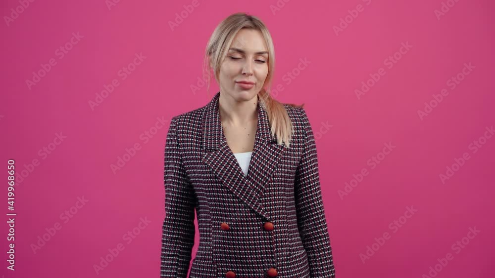 The discreet young woman looking at the camera shows the gesture of silence, She promises to keep it a secret. Beautiful young mature blonde in pink jacket. Isolated on a pink background. Concept of The discreet young woman looking at the camera shows the gesture of silence, She promises to keep it a secret. Beautiful young mature blonde in pink jacket. Isolated on a pink background. Concept of