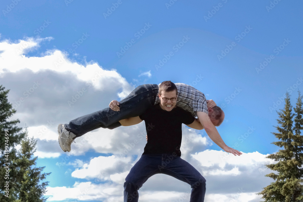 great togetherness with adult son carrying his dad across his shoulders and laughing. great togetherness with adult son carrying his dad across his shoulders and laughing.