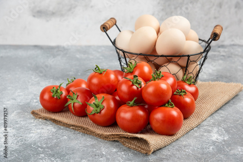 Fototapeta Naklejka Na Ścianę i Meble -  Basket of fresh uncooked eggs and ripe tomatoes on marble background