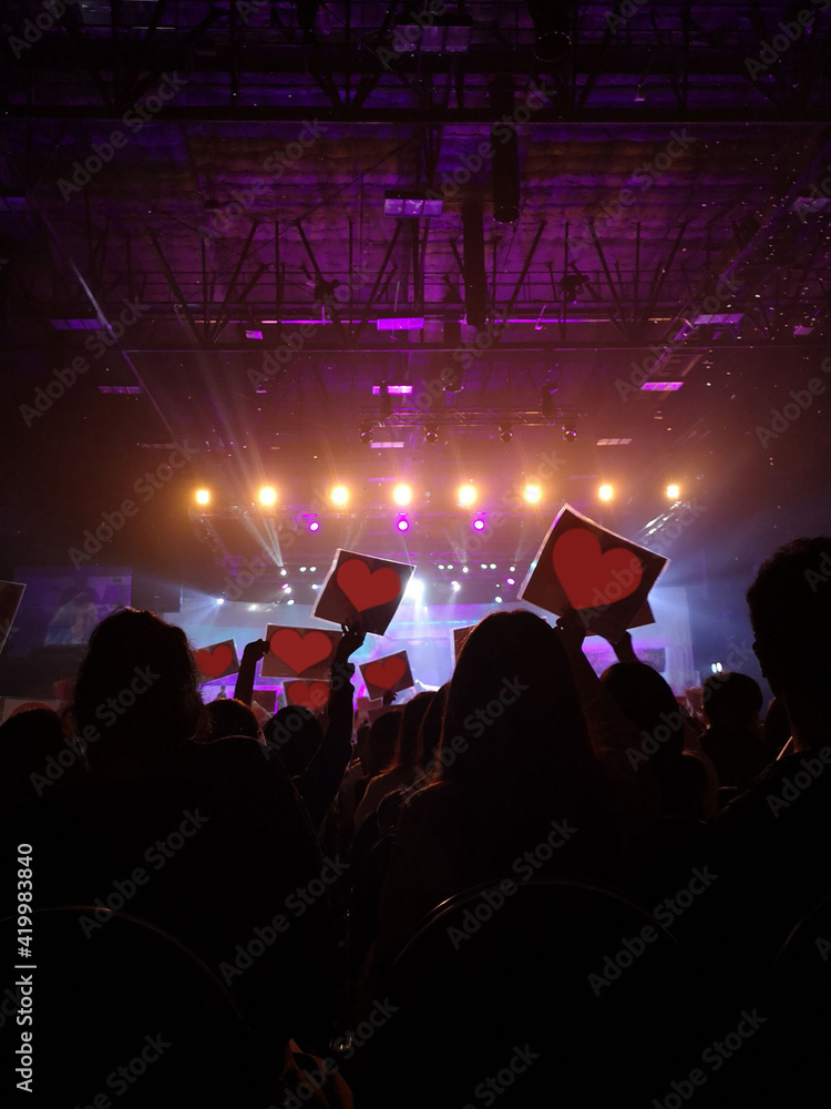 Blurred crowd at concert : Silhouette people crowd or fan club love, happy and cheering with led foam stick light in front of bright colourful stage lights. Soft focus.	


