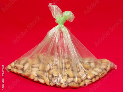 Pistachios in a plastic bag on a red background. © schankz