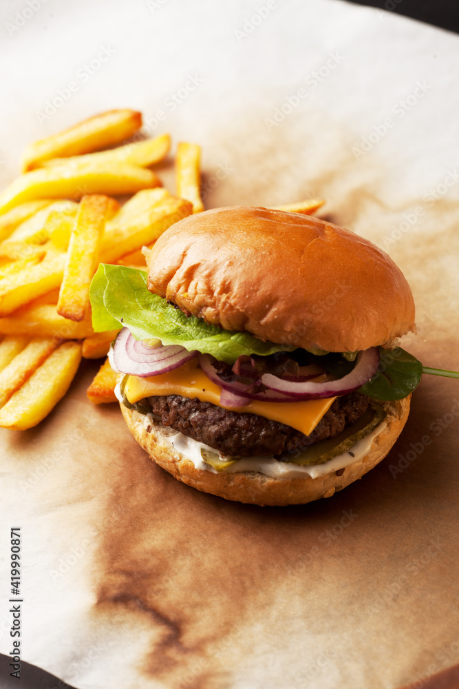 Tasty home made burger served with crispy fries. Rustic hamburger and potato chips composition with baking paper and wooden table. Tasty home made burger served with crispy fries. Rustic hamburger and potato chips composition with baking paper and wooden table.