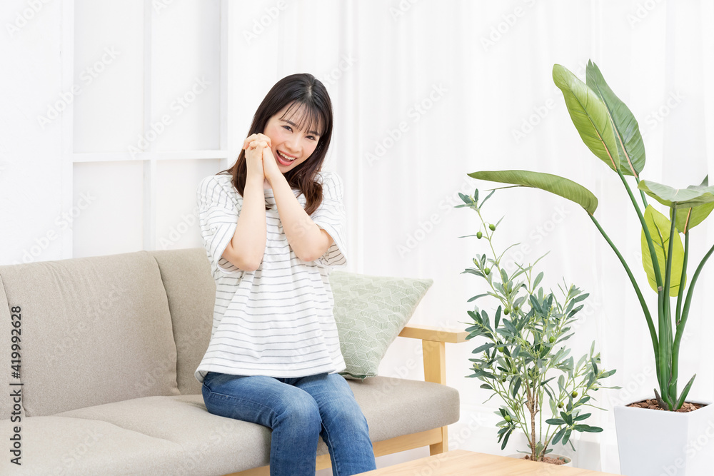 部屋のソファーに座ってお願いのジェスチャーをする若い女性 部屋のソファーに座ってお願いのジェスチャーをする若い女性