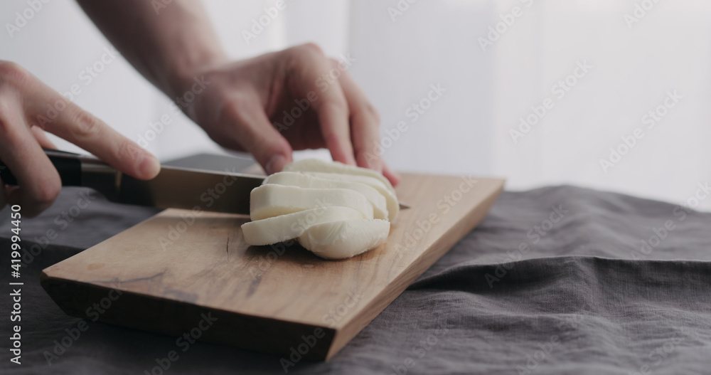 man slicing mozzarella ball on olive wood board with window on background