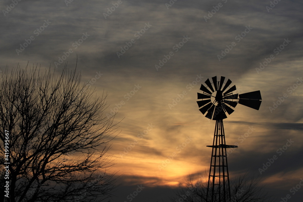 Kansas Windmill silhouette with a tree and colorful sky with clouds north of Hutchinson Kansas USA out in the country.