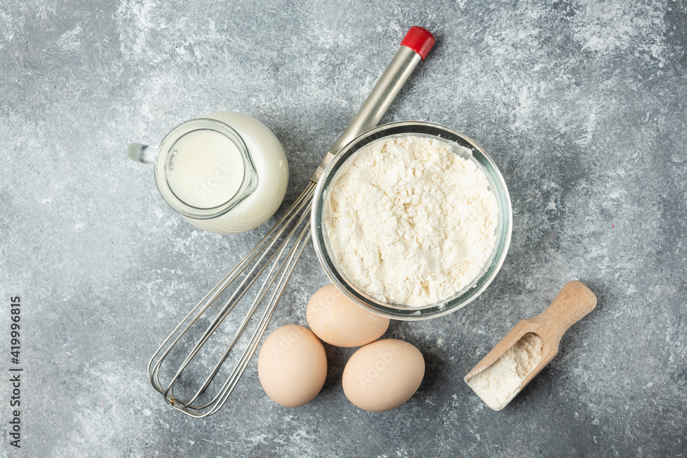 Flour, eggs, milk and whisker on marble background Flour, eggs, milk and whisker on marble background