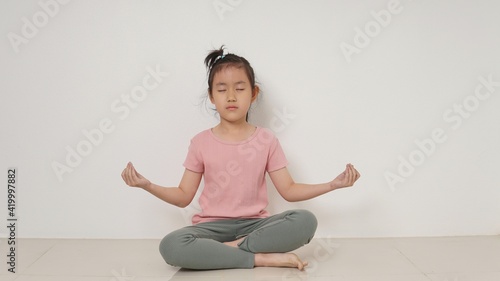 Happy little girl meditates at wall. Isolated on white background.
