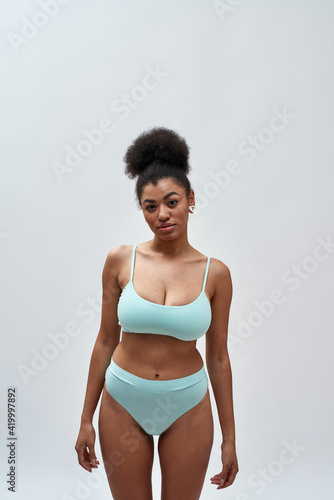 Beautiful sexy young mixed race woman wearing blue underwear looking at camera while posing isolated over light background