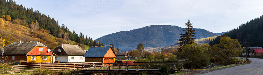 A small village located in a mountain valley. Autumn mountain landscape in the Ukrainian Carpathians - yellow and red trees combined with green needles.