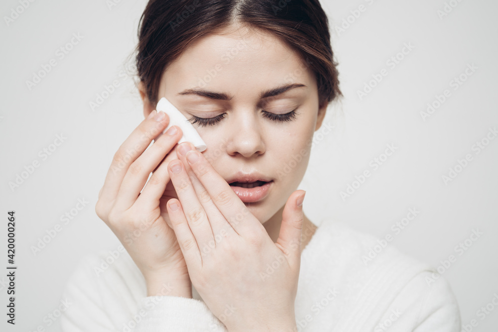 brunette woman wipes her face with a white sponge on a light background brunette woman wipes her face with a white sponge on a light background