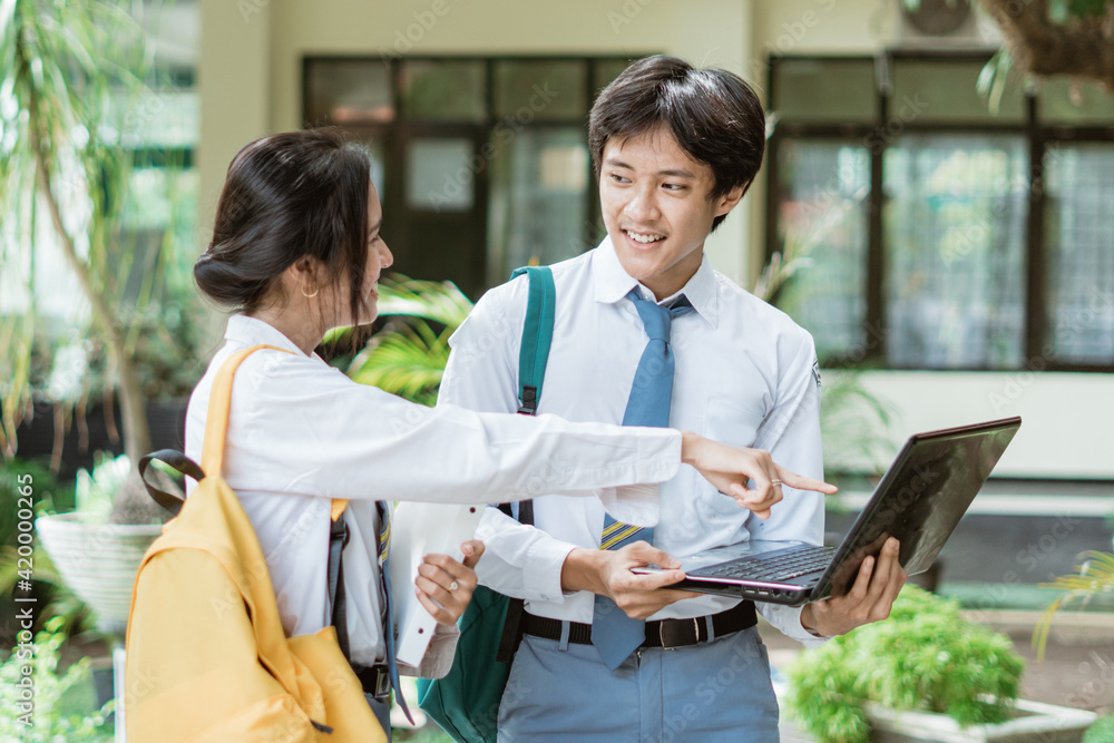 Obraz premium a couple of high school students standing wearing a bag while using a laptop computer together with finger pointing to screen