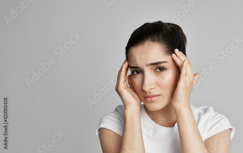 A woman in a white t-shirt holds her face with a headache and nigative health © SHOTPRIME STUDIO