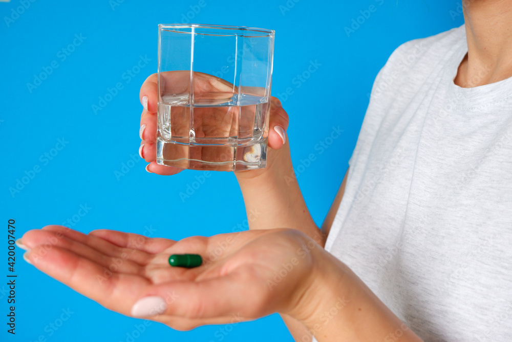 The medicine. The woman takes a pill. Tablet and glass of water in female hands on a blue background. Health care and people concept The medicine. The woman takes a pill. Tablet and glass of water in female hands on a blue background. Health care and people concept