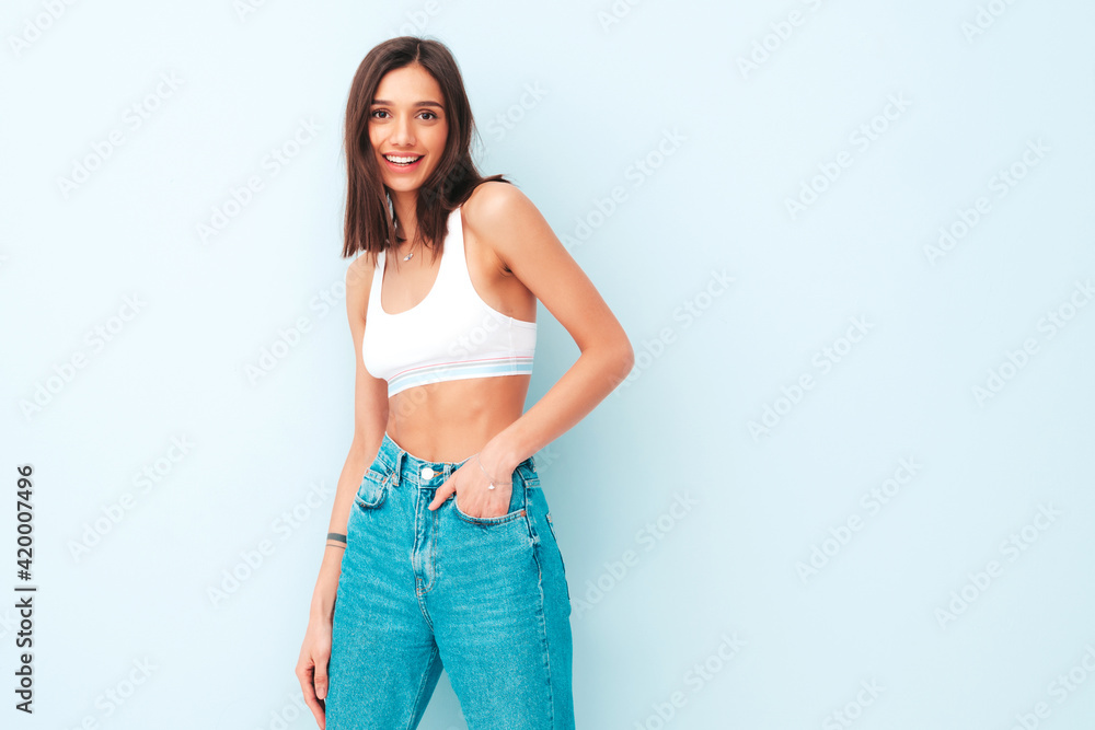 Beautiful smiling woman dressed in white jersey top shirt and jeans. Sexy carefree cheerful model enjoying her morning. Adorable and positive female posing near light blue wall in studio Beautiful smiling woman dressed in white jersey top shirt and jeans. Sexy carefree cheerful model enjoying her morning. Adorable and positive female posing near light blue wall in studio