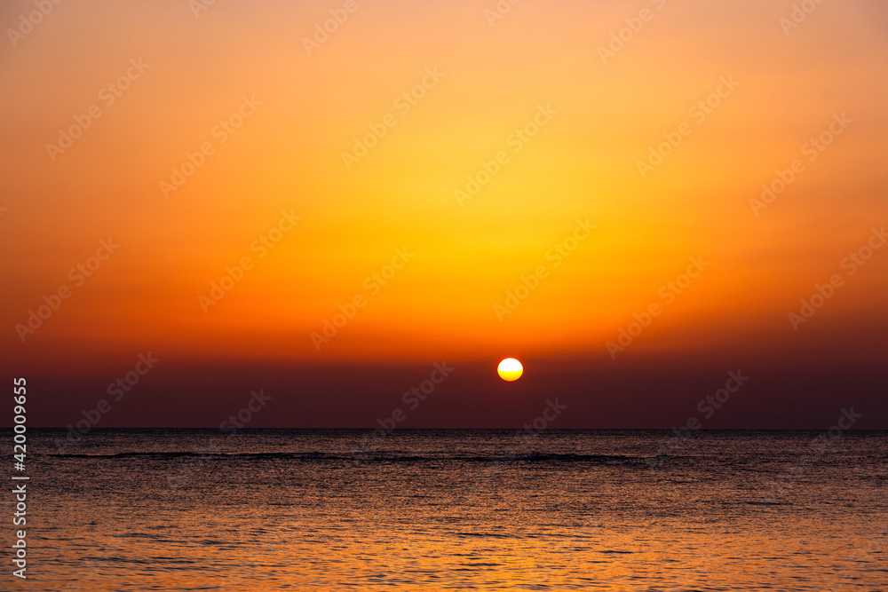 Bright sunset with a big yellow sun under the sea surface.