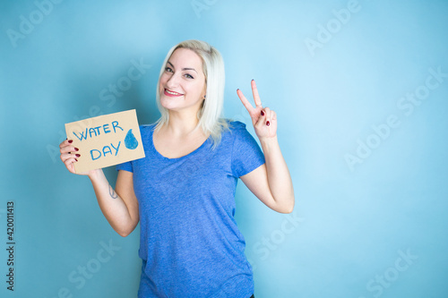 Young beautiful woman asking for the environment holding banner with water day message showing and pointing up with fingers number two while smiling confident and happy © Irene